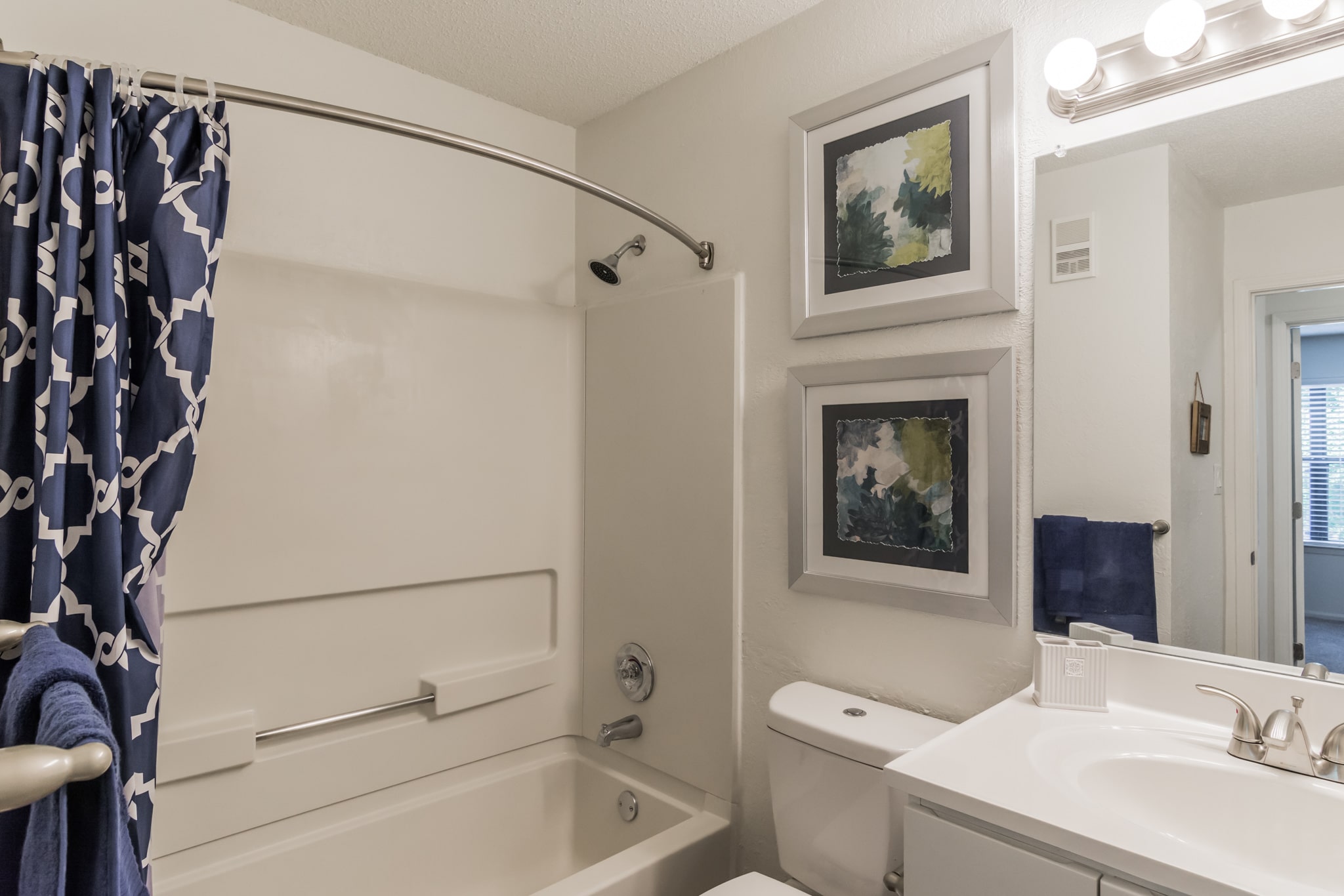 A white bathroom with a blue shower curtain in a Two Bedroom Apartment.